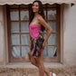 Tropical silk sarong worn as a skirt in dark khaki, bright pink and copper tones, on a woman in pink bathing suit infront of a beige awning.