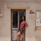 Woman in a pink bathing suit standing in front of an old building with a wooden door, with a silk sarong.