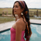 Tropical silk sarong worn as a head scarf in dark khaki, bright pink and copper tones, on a woman in pink bathing suit.