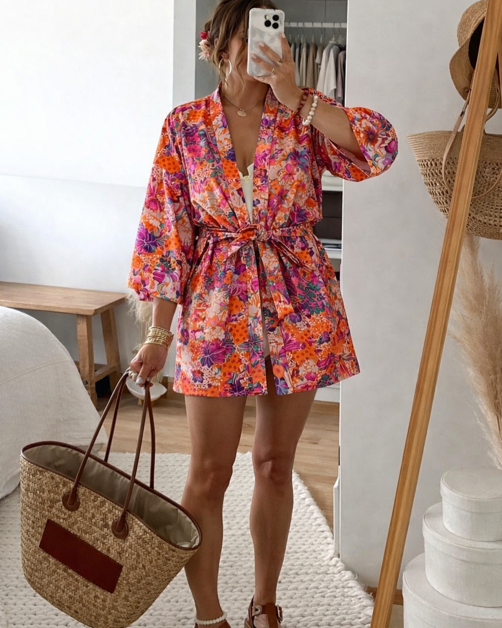 Person wearing a colorful floral kimono holding a straw bag indoors.